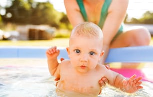Little baby boy with his unrecognizable mother in the swimming pool in the garden. Summer time.