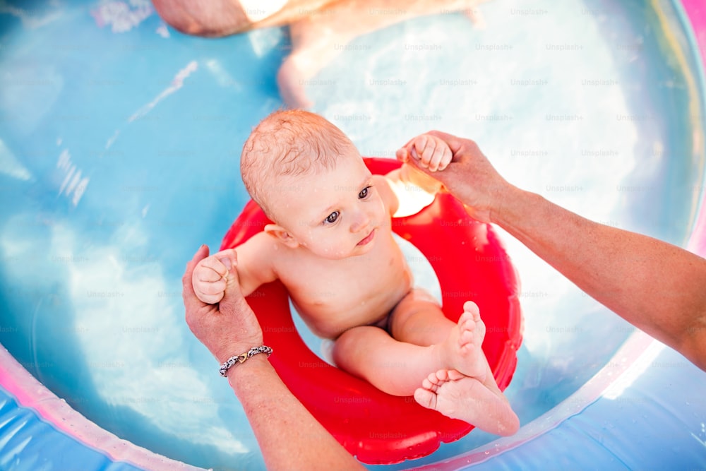 Menino pequeno com seu pai irreconhecível na piscina no jardim. Horário de verão.