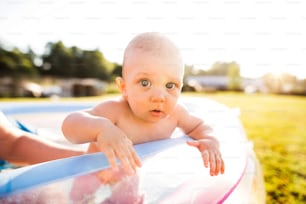 Little baby boy with his unrecognizable parent in the swimming pool in the garden. Summer time.