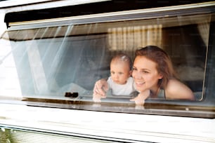 Beautiful young mother and her baby son in a camper van on a summer day. Shot through glass.