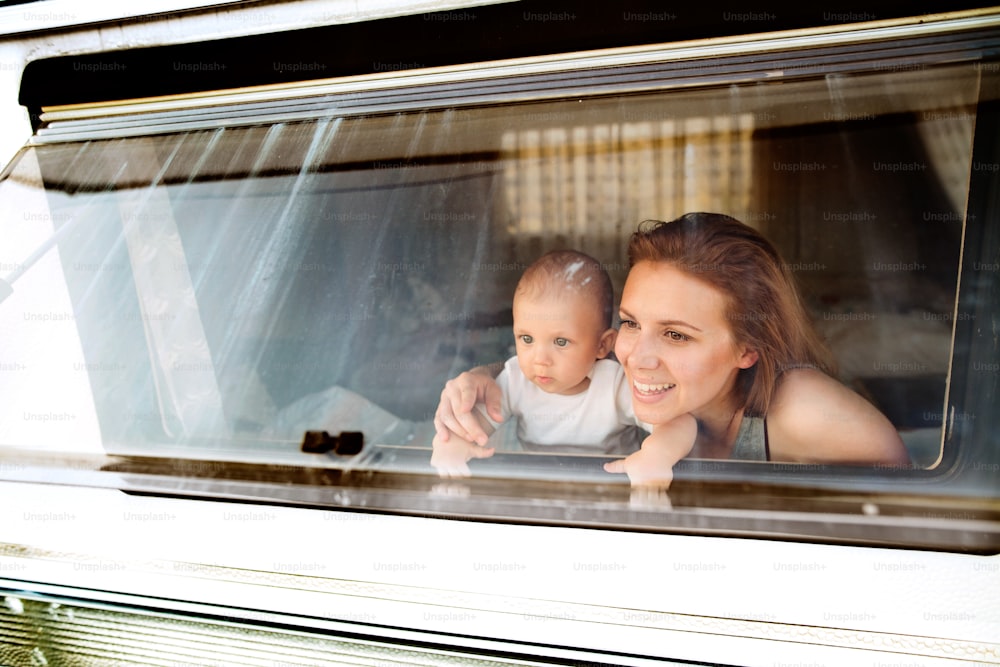 Beautiful young mother and her baby son in a camper van on a summer day. Shot through glass.
