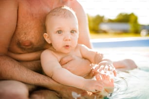 Little baby boy with his unrecognizable father in the swimming pool in the garden. Summer time.
