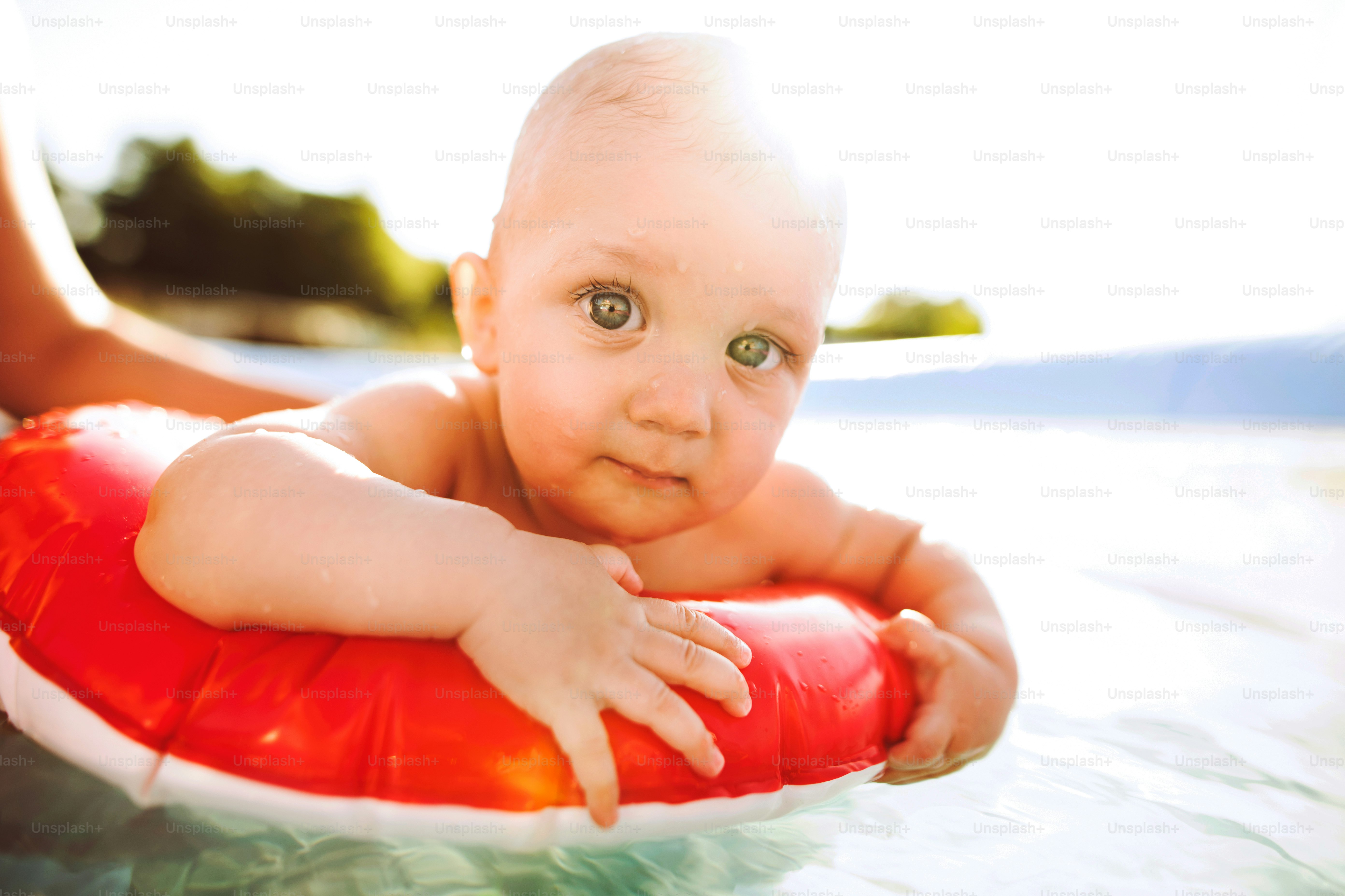 Little baby boy with his unrecognizable mother in the swimming pool in the garden. Summer time.