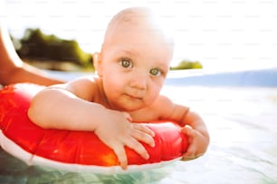 정원의 수영장에서 알아볼 수 없는 어머니와 함께 있는 어린 아기. 여름철.