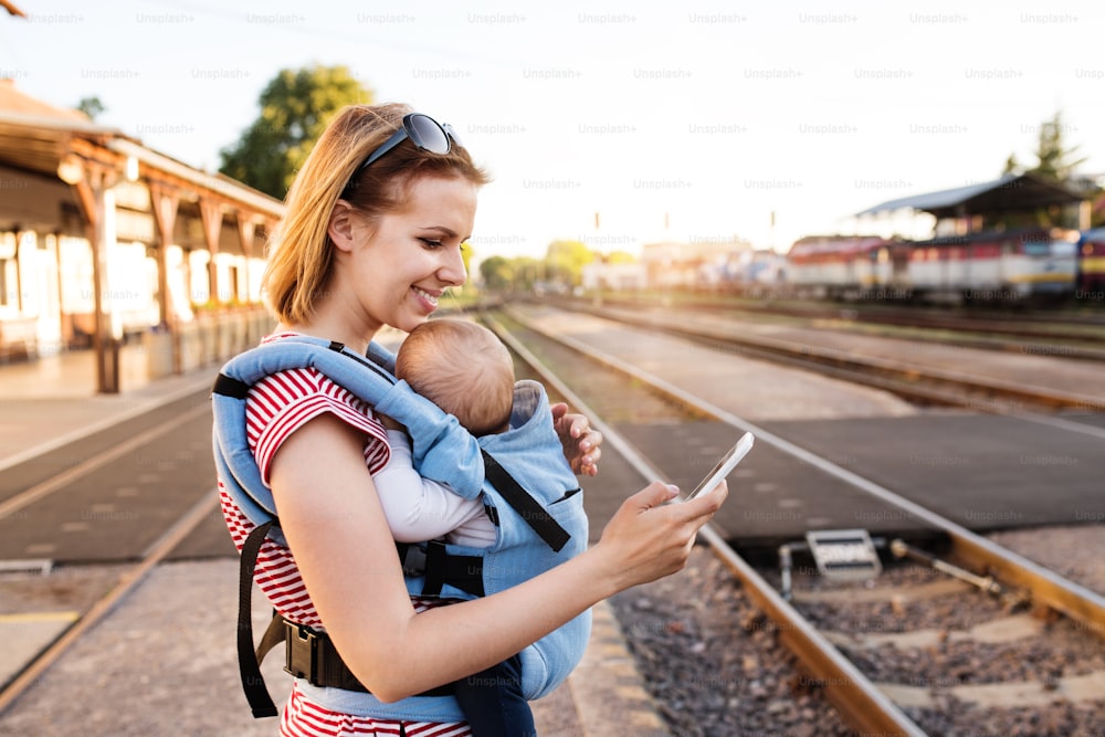 Madre joven que viaja con un bebé en tren. Una mujer con un smartphone y su hijo en la estación de tren.
