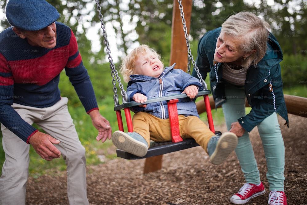 Senior couple with grandson at the playground. Little boy on the swing, crying.