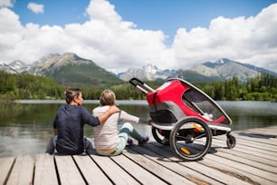 Senior couple and children in jogging stroller, summer day. High mountains in the background. Rear view.