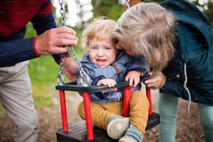 Unrecognizable senior couple with grandson at the playground. Little boy on the swing.