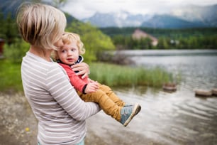 Senior woman with little boy at the lake, summer day. High mountains in the background.
