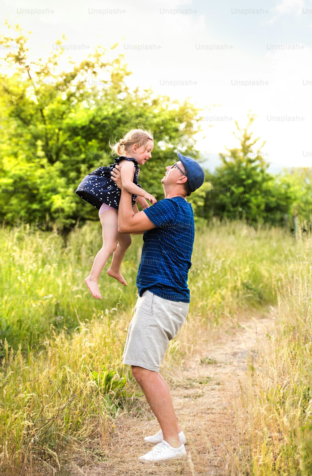 緑の夏の自然の中で、かわいい娘を空中に高く抱きしめる若い父親。