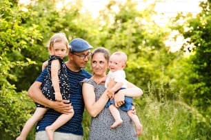 Familia joven feliz con niños pequeños que pasan tiempo juntos al aire libre en la naturaleza verde del verano