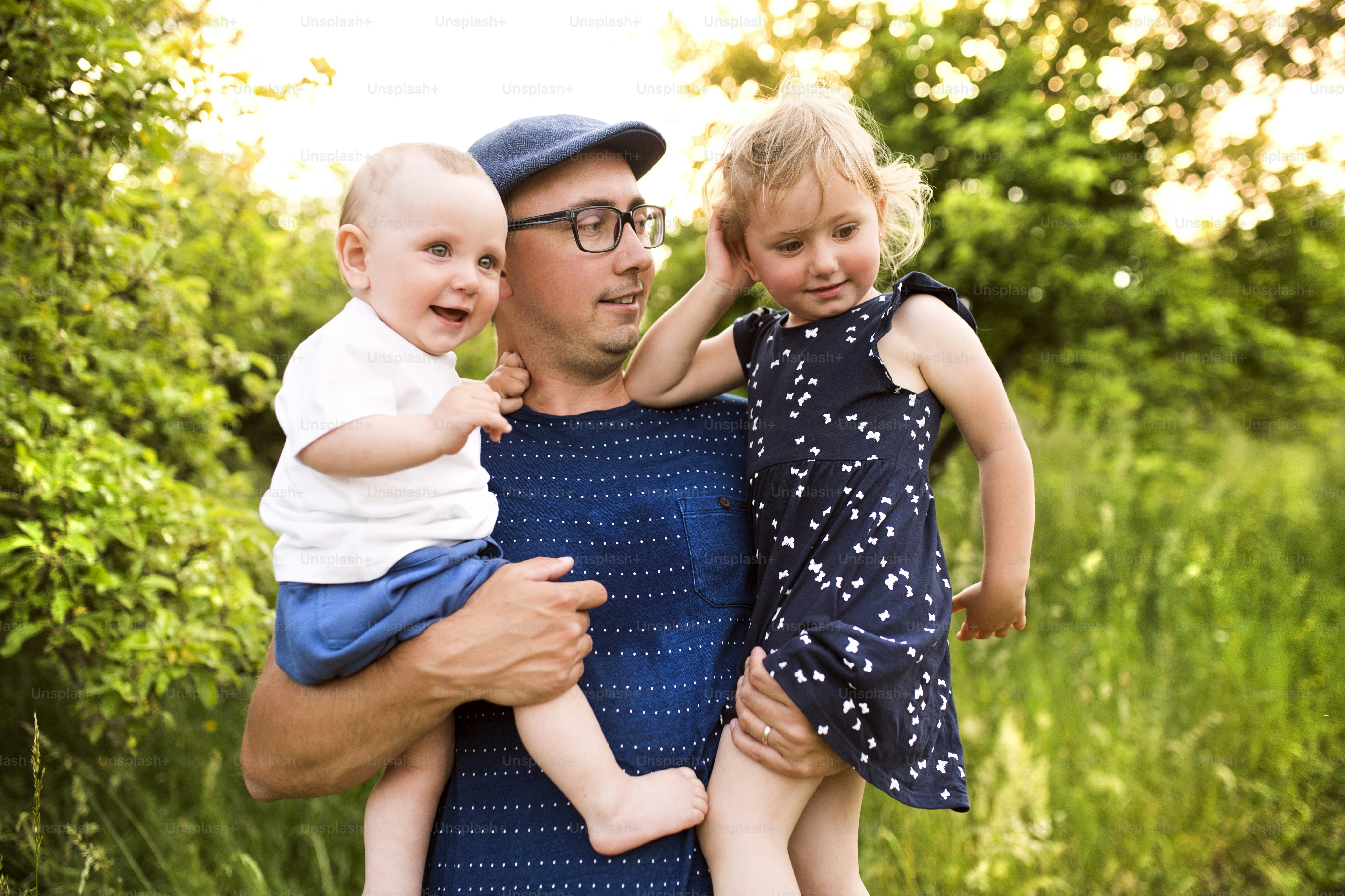 Happy young father with little children spending time together outside in green summer nature