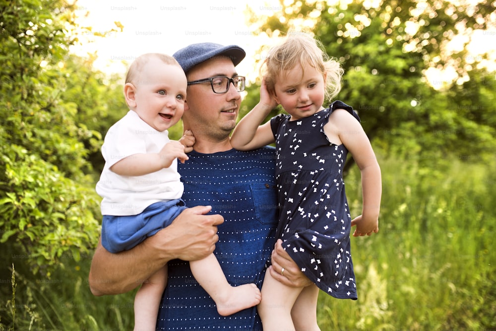 Padre joven feliz con niños pequeños que pasan tiempo juntos al aire libre en la naturaleza verde del verano