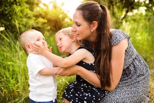 Beautiful young mother with little children spending time together outside in green summer nature.