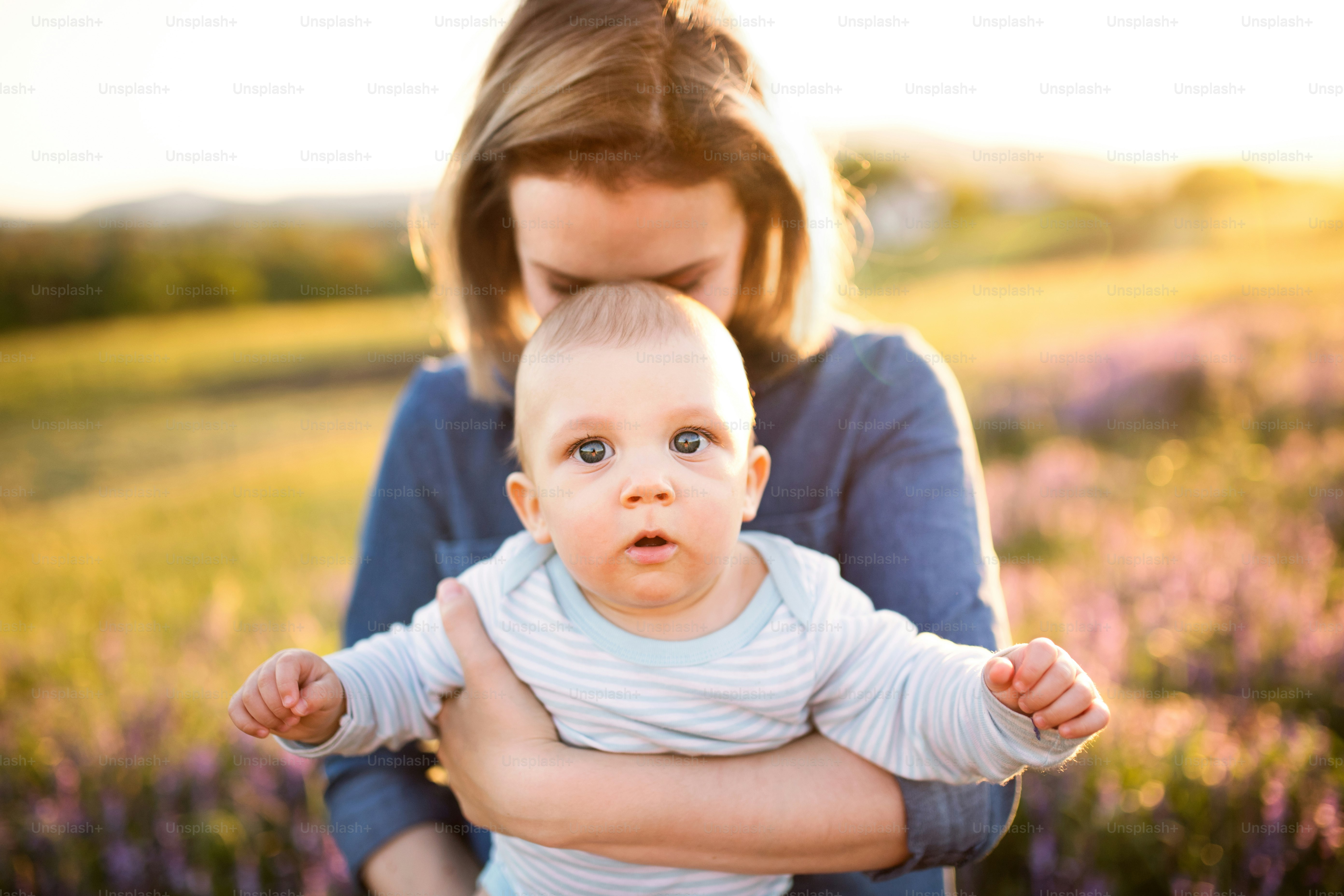 Ibu muda yang cantik menggendong bayi laki-lakinya yang masih kecil di pelukan di luar ruangan di alam di ladang lavender.