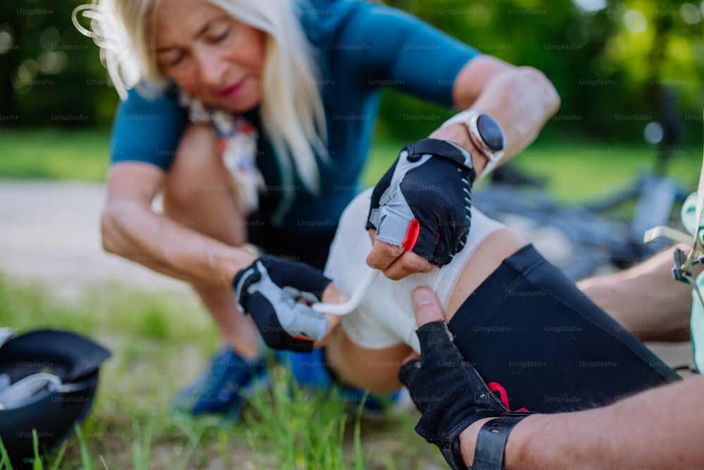 Uma mulher idosa está ajudando o homem depois que ele caiu da bicicleta no chão e machucou o joelho, no parque no verão.