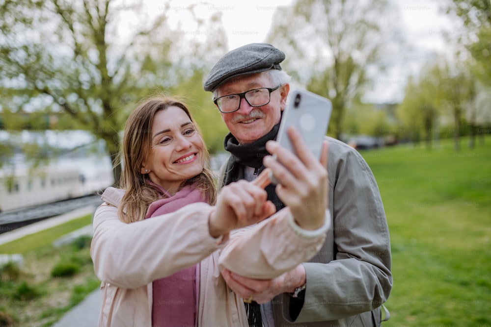 Un hombre mayor feliz y su hija adulta tomándose selfies al aire libre en un paseo por el parque.