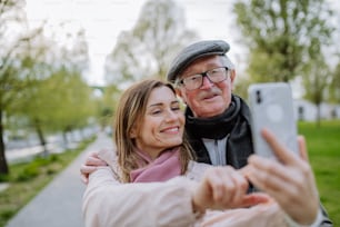 Um homem idoso feliz e sua filha adulta tirando selfie ao ar livre em uma caminhada no parque.