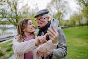 Un hombre mayor feliz y su hija adulta tomándose selfies al aire libre en un paseo por el parque.