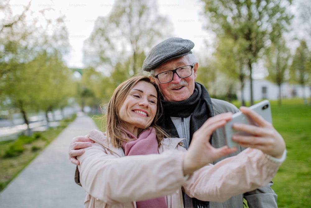 Un uomo anziano felice e sua figlia adulta che scattano selfie all'aperto durante una passeggiata nel parco.