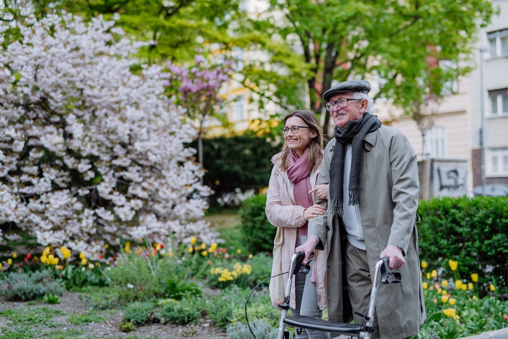 Un uomo anziano con deambulatore e figlia adulta all'aperto durante una passeggiata nel parco.