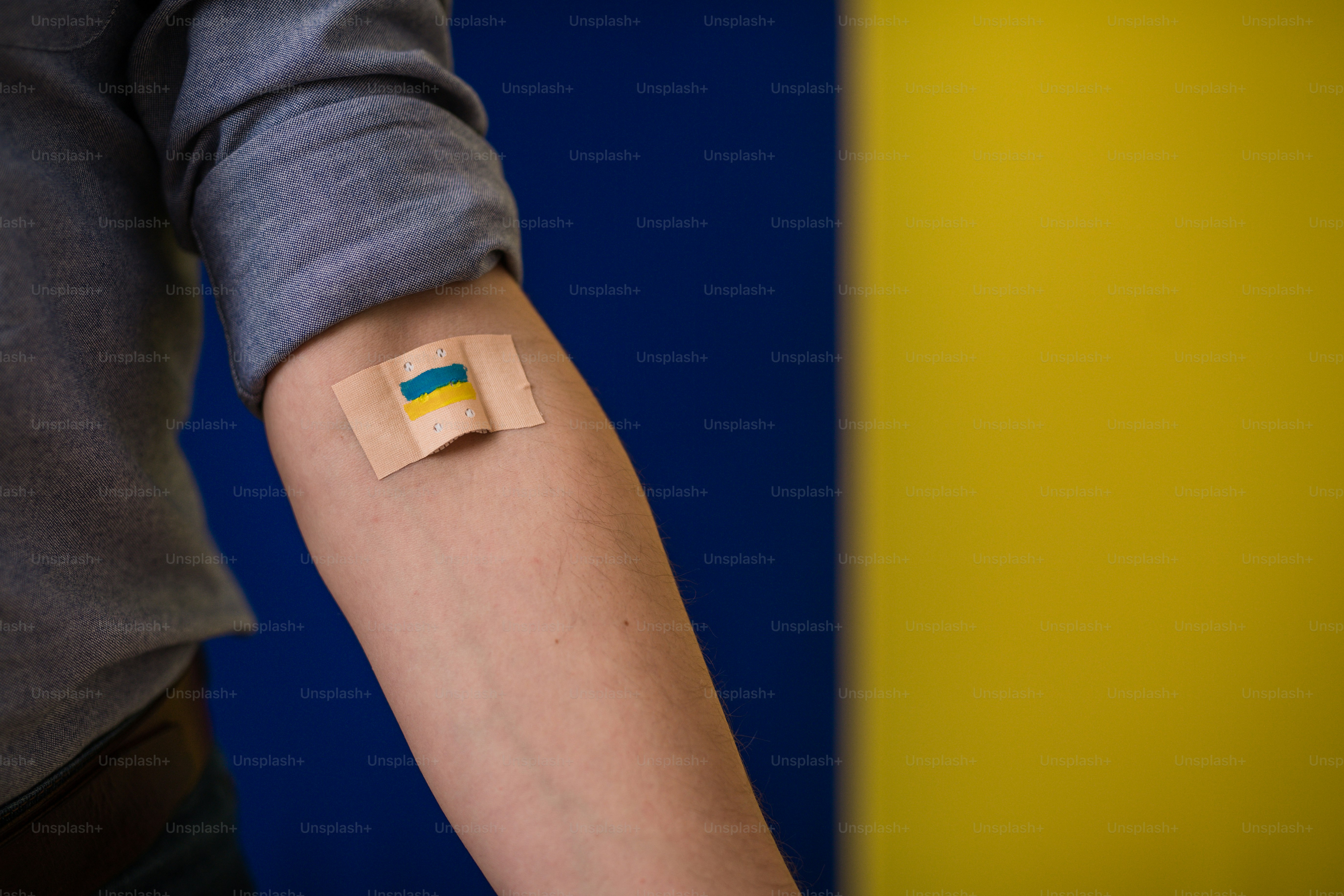 Blood donor with a bandage after giving blood on Ukrainian flag background.