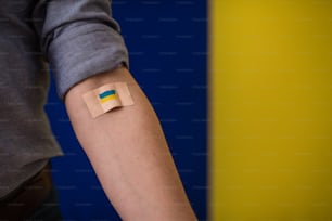 Blood donor with a bandage after giving blood on Ukrainian flag background.