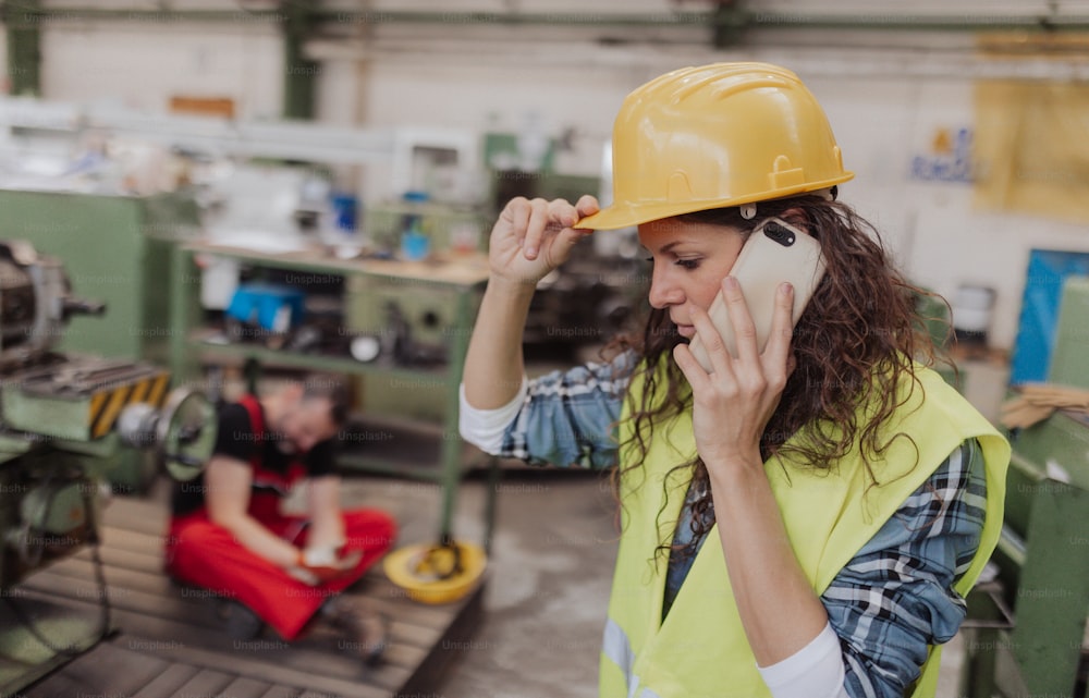 A woman is calling ambulance for her colleague after accident in factory. First aid support on workplace concept.