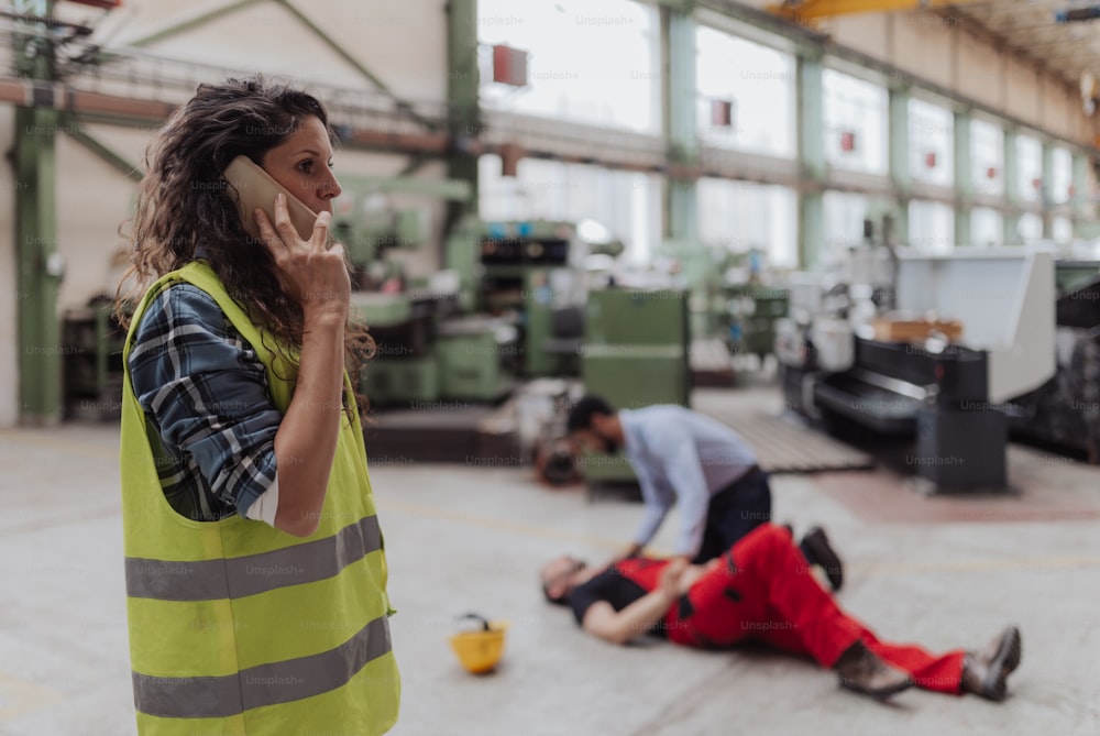 Una donna sta chiamando l'ambulanza per il suo collega dopo un incidente in fabbrica. Supporto di primo soccorso sul concetto di posto di lavoro.
