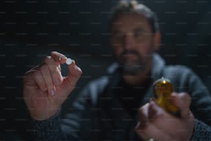A blurred man holding and showing drug pill on dark background, mental health concept.