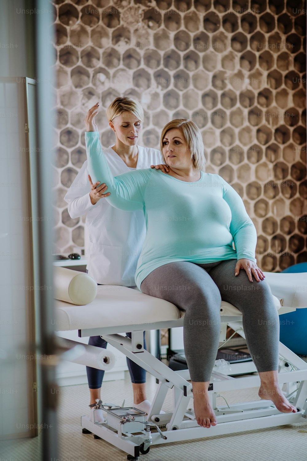 リハビリテーションセンターの屋内で太りすぎの女性と運動する中年の理学療法士の女性