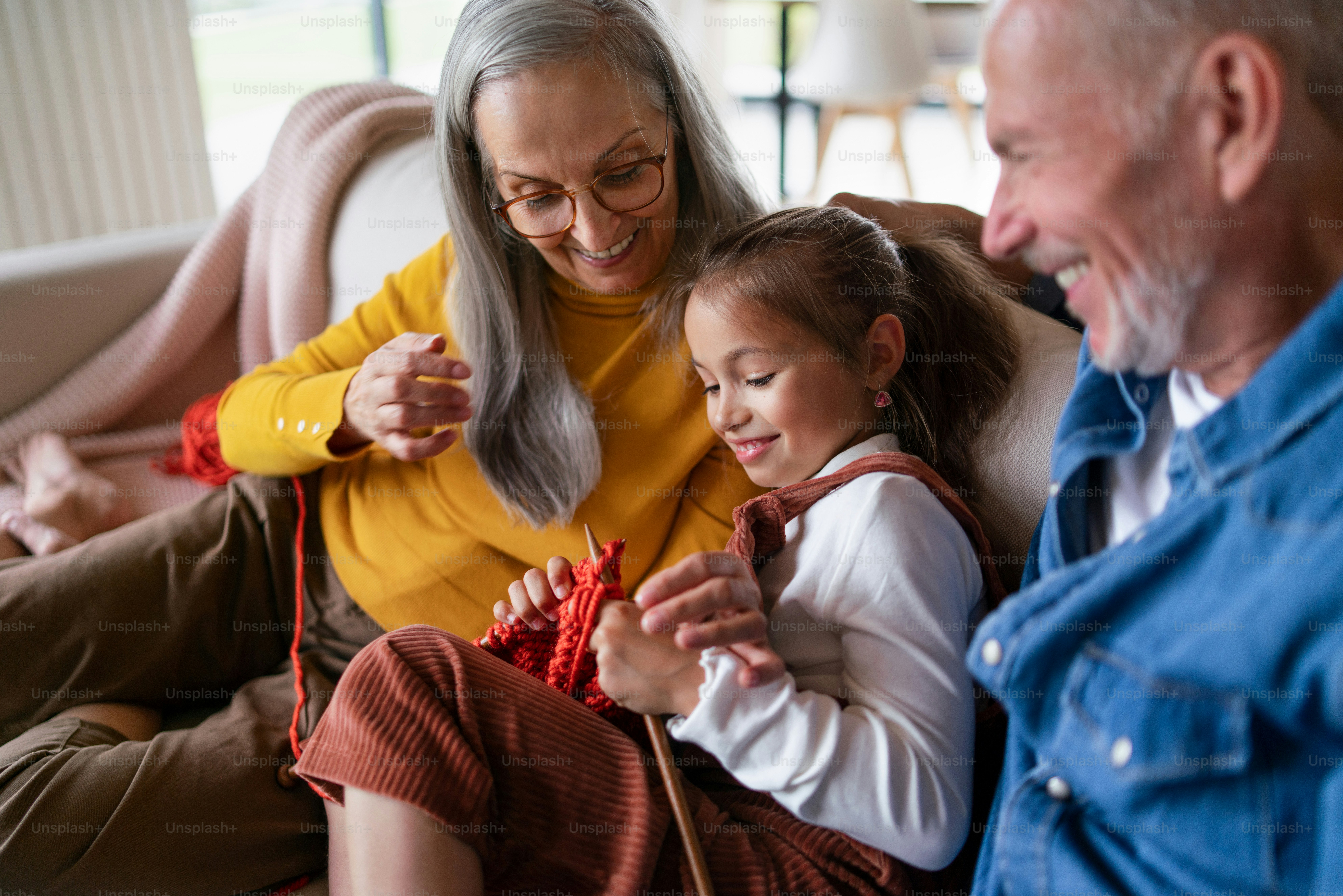 Una niña sentada en el sofá con sus abuelos y aprendiendo a tejer en el ...