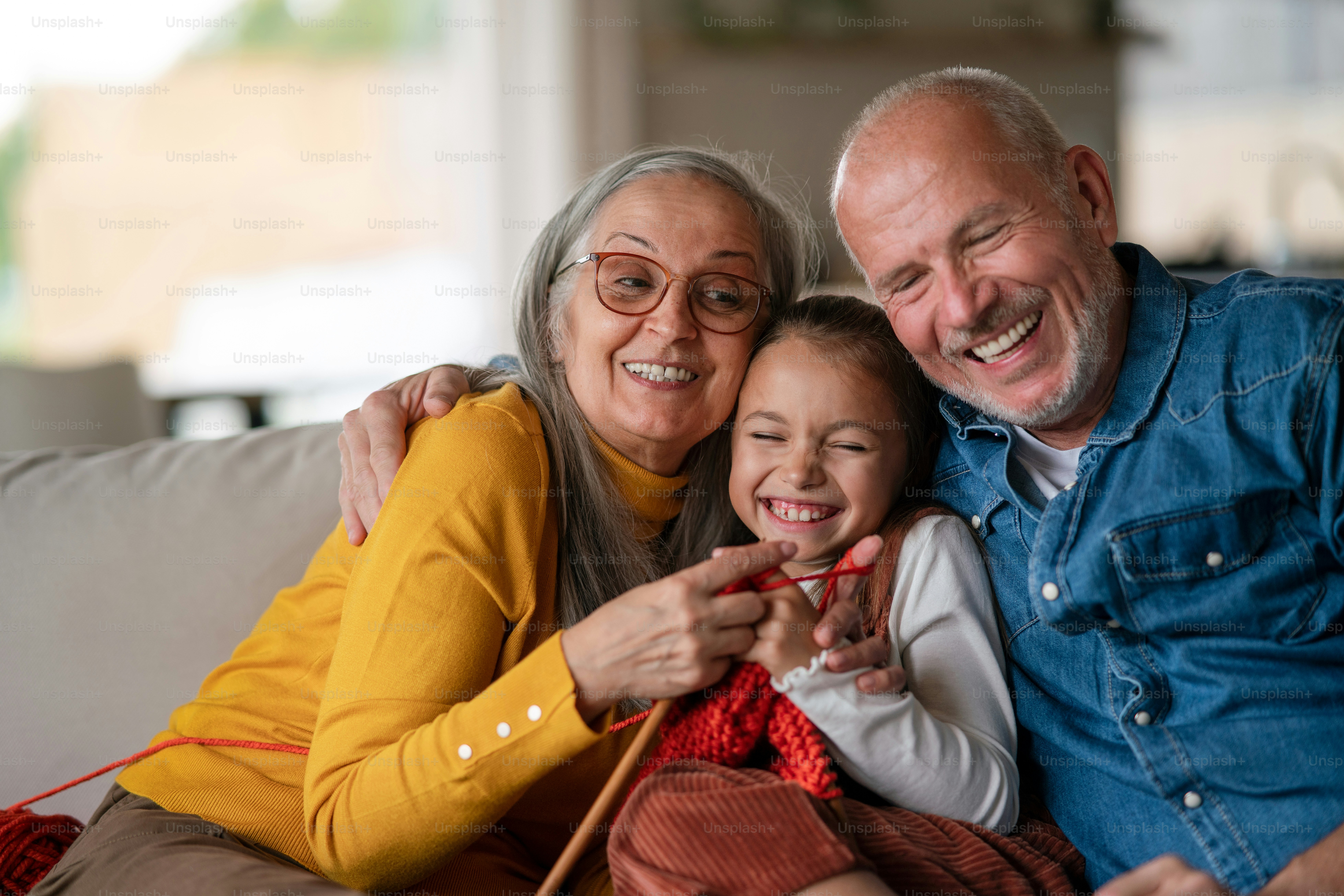 Una niña sentada en el sofá con sus abuelos y aprendiendo a tejer en el ...