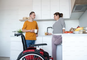 Mulher madura deficiente com perna amputada conversando com seu filho na cozinha dentro de casa.