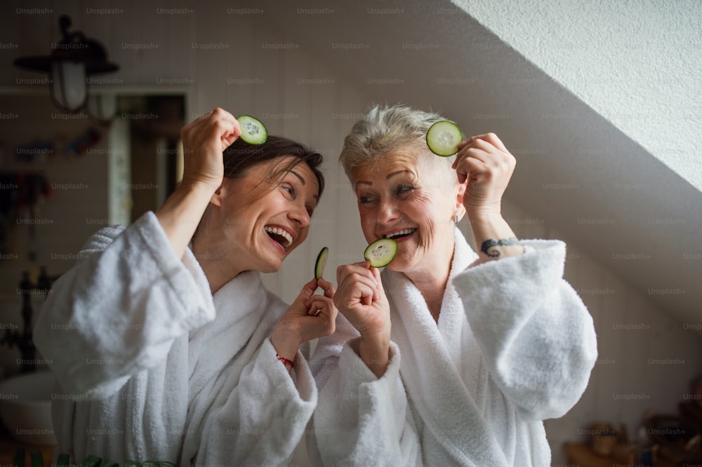 A happy senior mother in bathrobe with adult daughter indoors at home, selfcare concept.