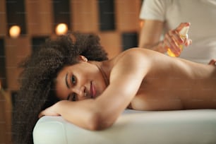 Mujer joven teniendo masaje relajante de espalda en el spa, mirando a la cámara.