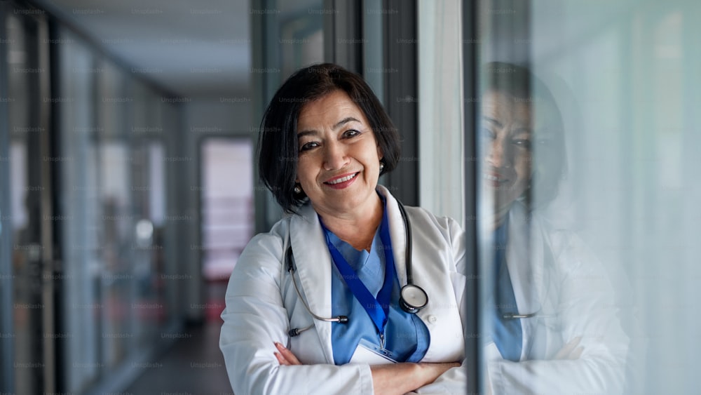 Front view portrait of senior woman doctor standing in hospital, looking at camera.