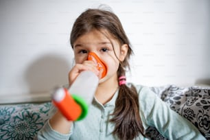 Un retrato de una niña pequeña enferma en casa, usando un inhalador.