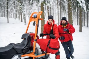 Man and woman paramedics from mountain rescue service provide operation outdoors in winter in forest.