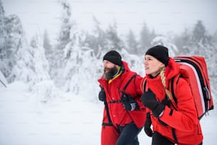 Paramedics from mountain rescue service walking and talking outdoors in winter in forest.
