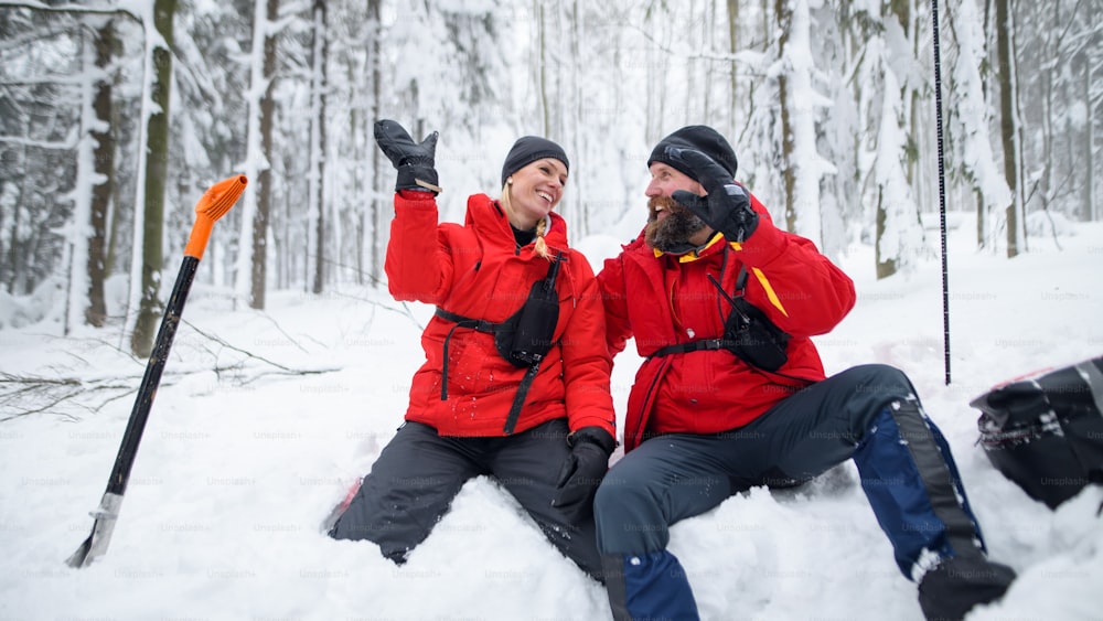 Servizio di soccorso alpino in funzione all'aperto in inverno nel bosco, scavando neve con pale e dando figh cinque.