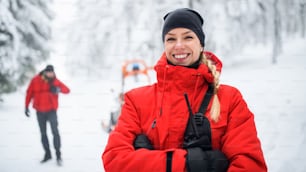 Retrato de una mujer paramédica del servicio de rescate de montaña al aire libre en invierno en el bosque, mirando a la cámara.