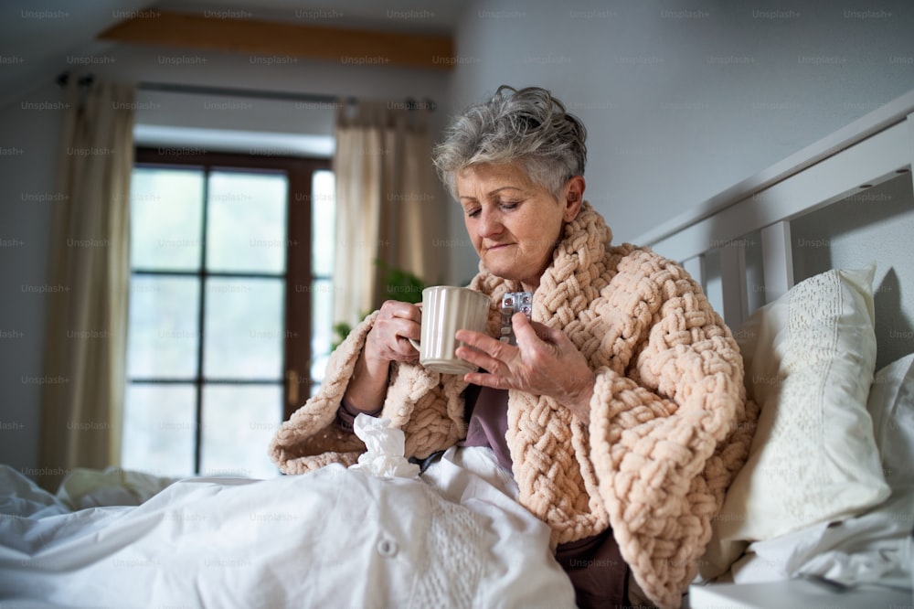 Uma mulher idosa doente na cama em casa, tomando medicação. Efeitos colaterais pós-vacinação.