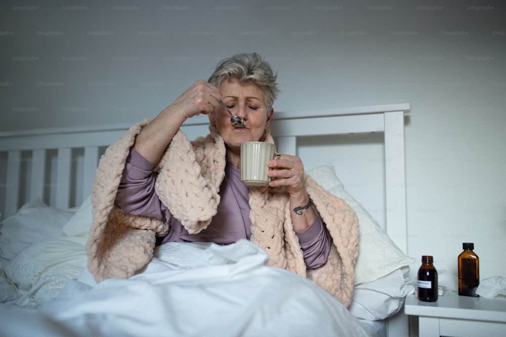 Une femme âgée malade au lit à la maison, prenant des médicaments.