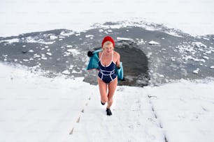 젖은 수영복을 입은 활동적인 노인 여성이 겨울에 야외에서 계단을 오르는 모습, 냉찜질 개념.