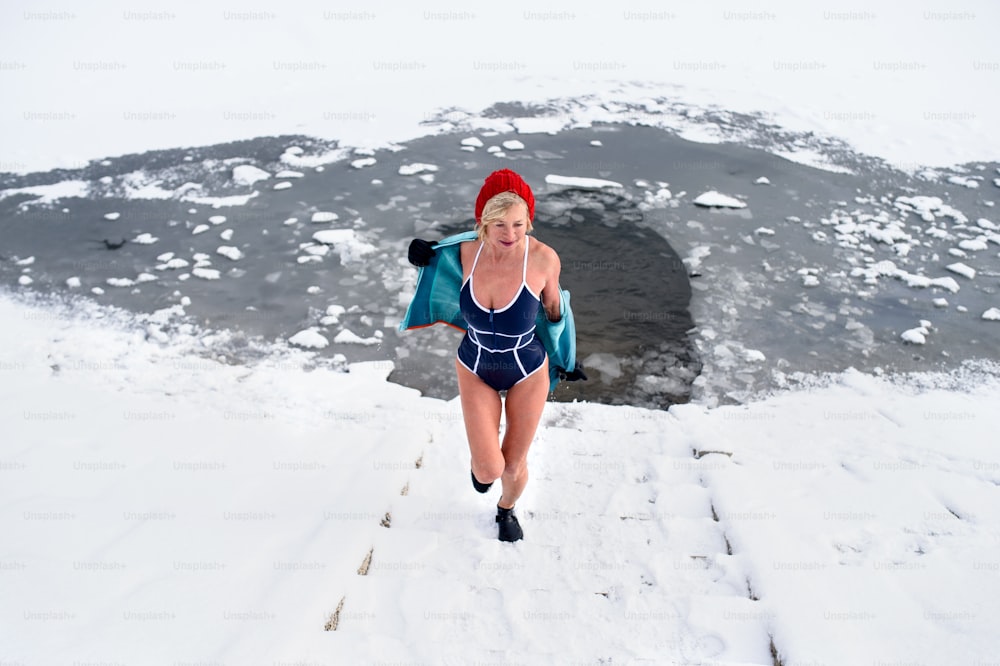 High angle view of an active senior woman in wet swimsuit running up stairs outdoors in winter, cold therapy concept.