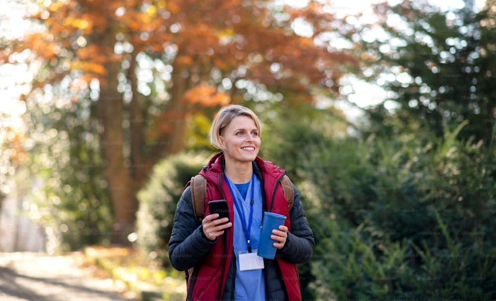 Retrato de una mujer cuidadora, enfermera o trabajadora de la salud al aire libre de camino al trabajo, usando un teléfono inteligente.