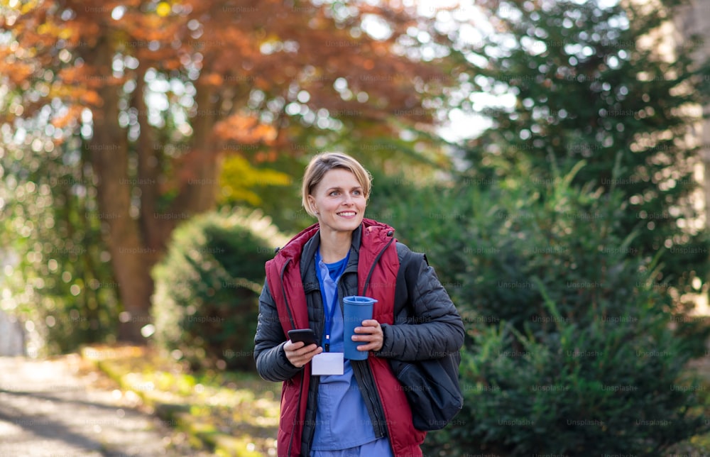 Retrato de una mujer cuidadora, enfermera o trabajadora de la salud al aire libre de camino al trabajo, usando un teléfono inteligente.