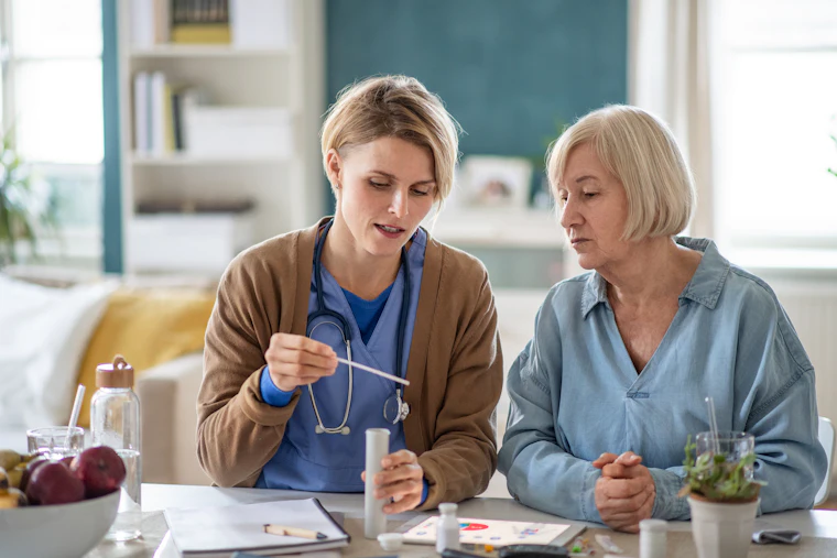 A carer sitting at a table with an older woman, going through her medication together