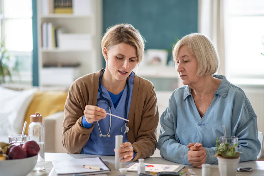 A carer sitting at a table with an older woman, going through her medication together